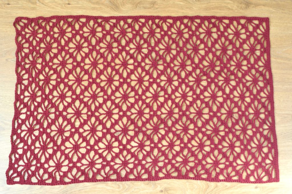 Flat lace crochet shrug pattern in red yarn with openwork design.