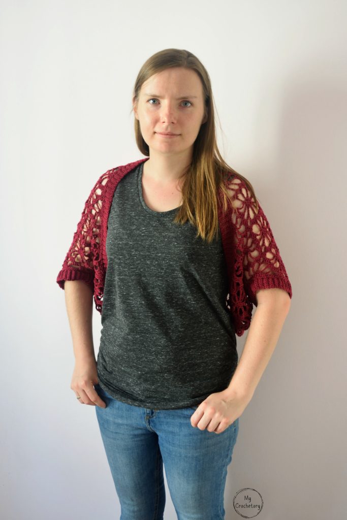 Model wearing lace crochet shrug pattern in red, front view.