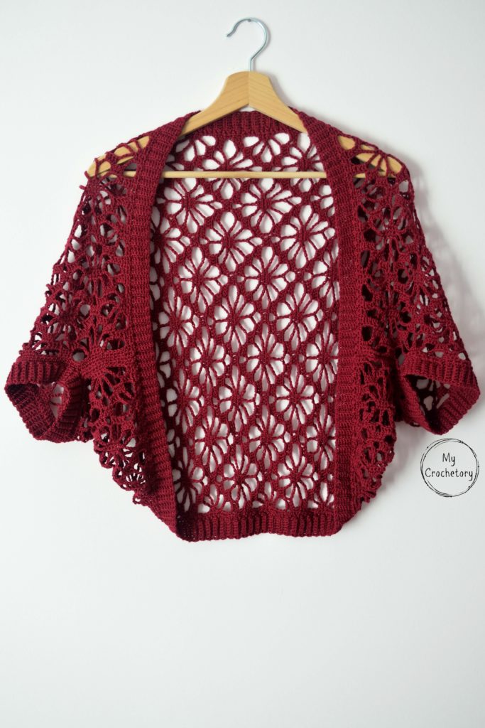 Finished crochet shrug pattern on a hanger, featuring lace design