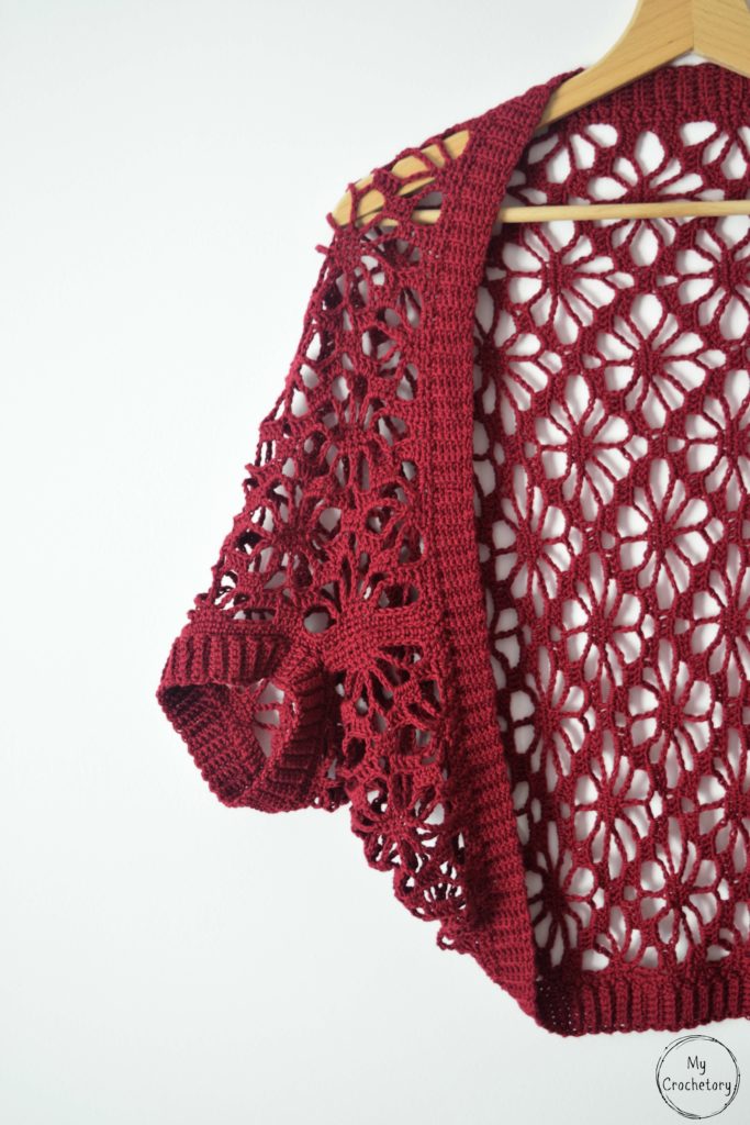 Lace crochet shrug pattern on a hanger, showcasing detailed sleeve and floral motifs