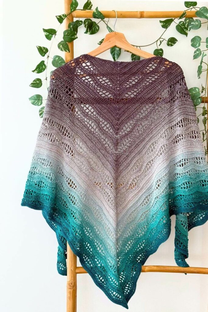 Kalinda Shawl crochet pattern – full triangle shawl with wavy stitch texture and gradient colors from purple to teal, displayed flat on bamboo rack by MyCrochetory.