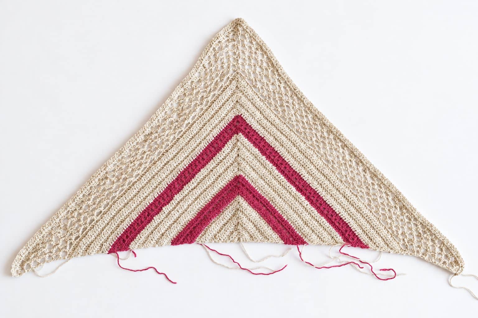 Triangle of the Spring Solstice Wrap laid flat before the side panels, with pink stripes and yarn ends still hanging