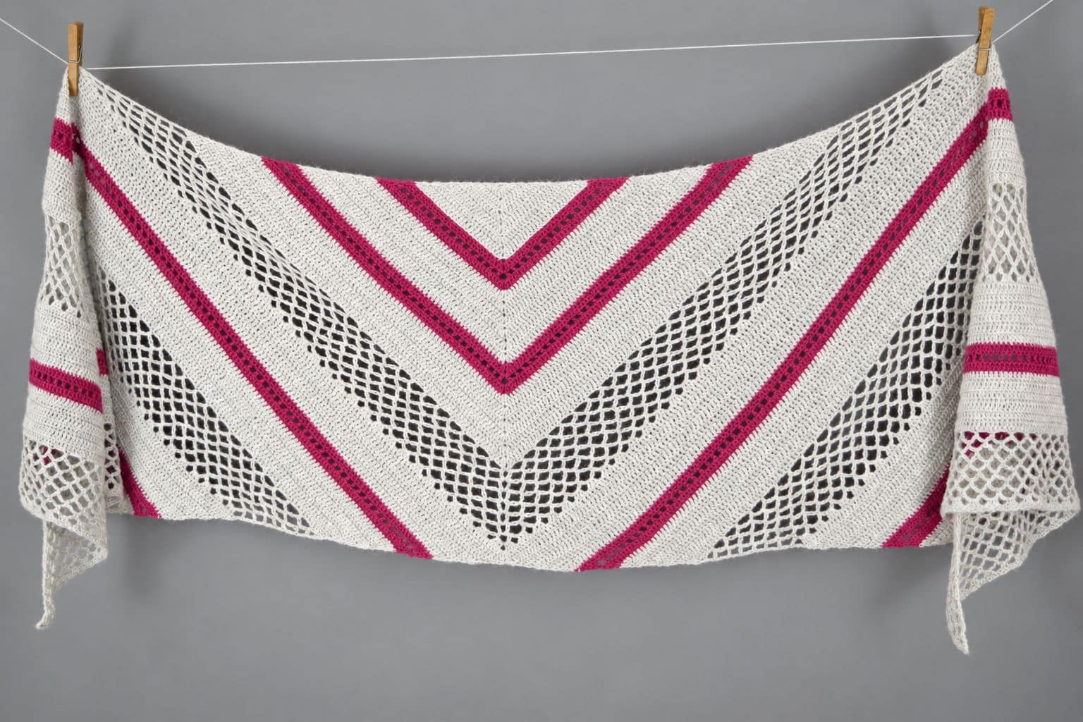 The whole Spring Solstice Wrap laid flat, a crochet trapezoid shawl with mesh lace and pink eyelet stripes