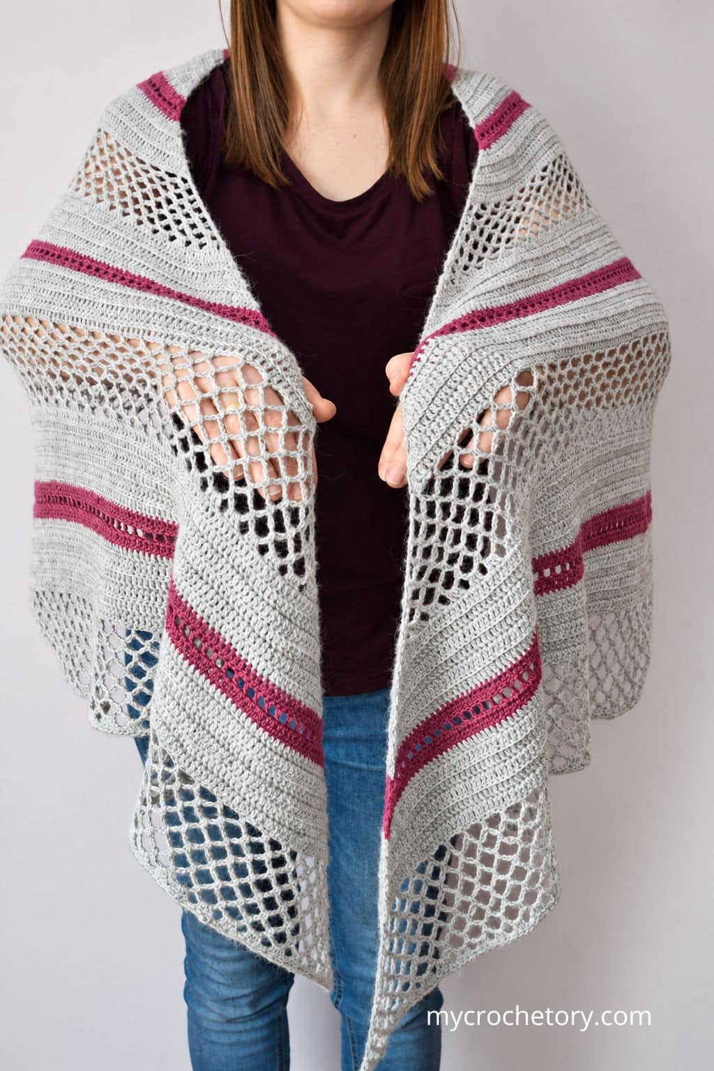 Woman wearing the Spring Solstice Wrap, a crochet trapezoid shawl in light gray with dark pink stripes