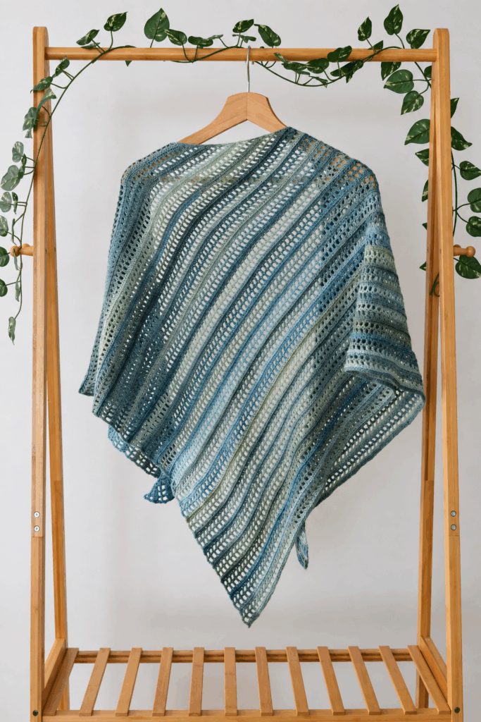 imple crochet shawl Aprilis draped over a wooden hanger on a bamboo clothes rack, showing the full triangle shape