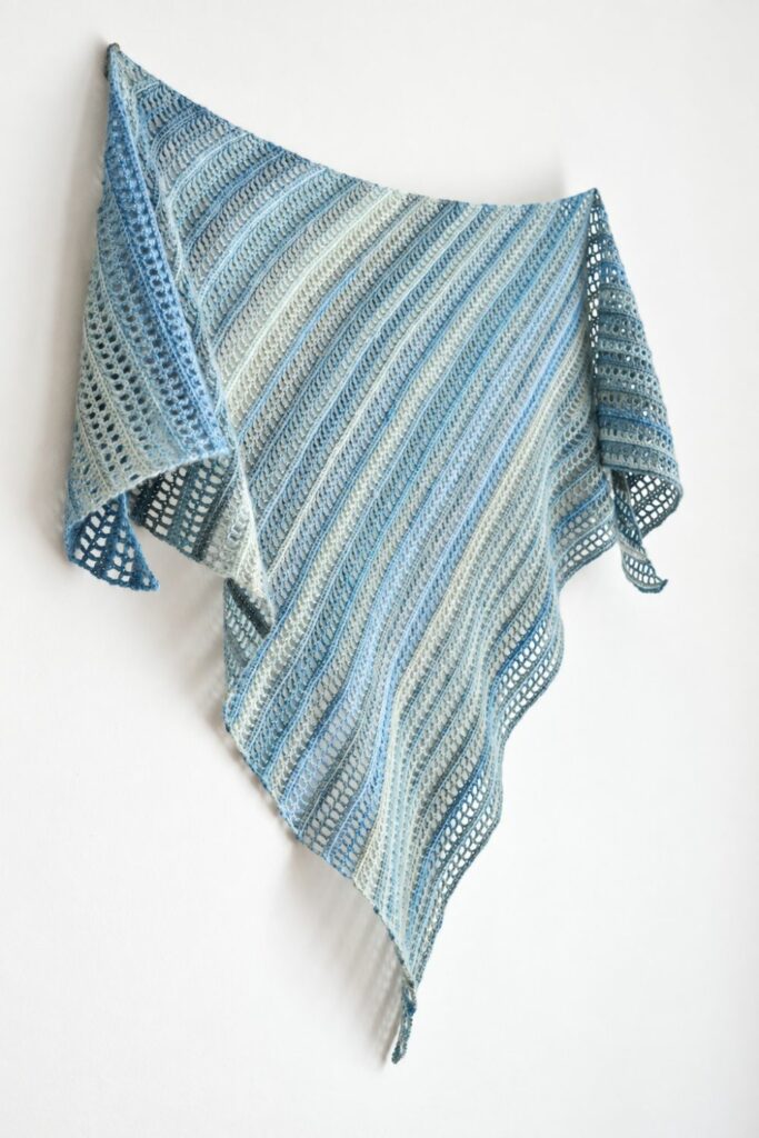 Simple crochet shawl Aprilis hanging on a wall, the diagonal stripes running down to the long tip