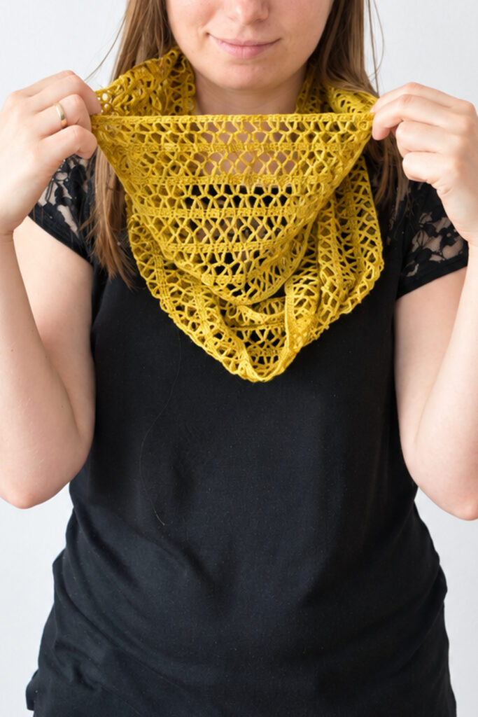 rochet lace cowl in ochre lace weight yarn, held open in front of a black lace top