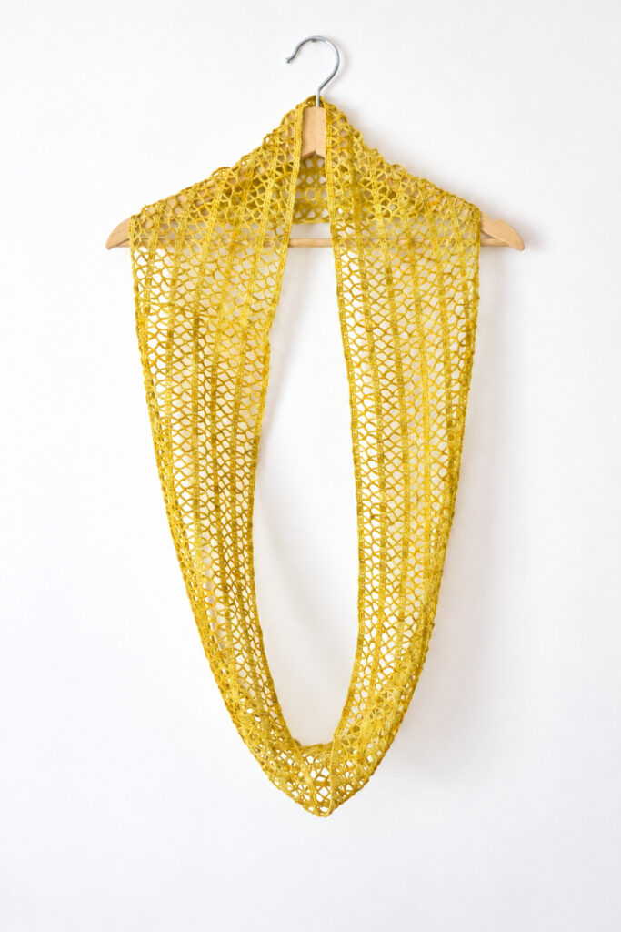 Lace infinity scarf in ochre hanging long from a wooden hanger, showing the full loop