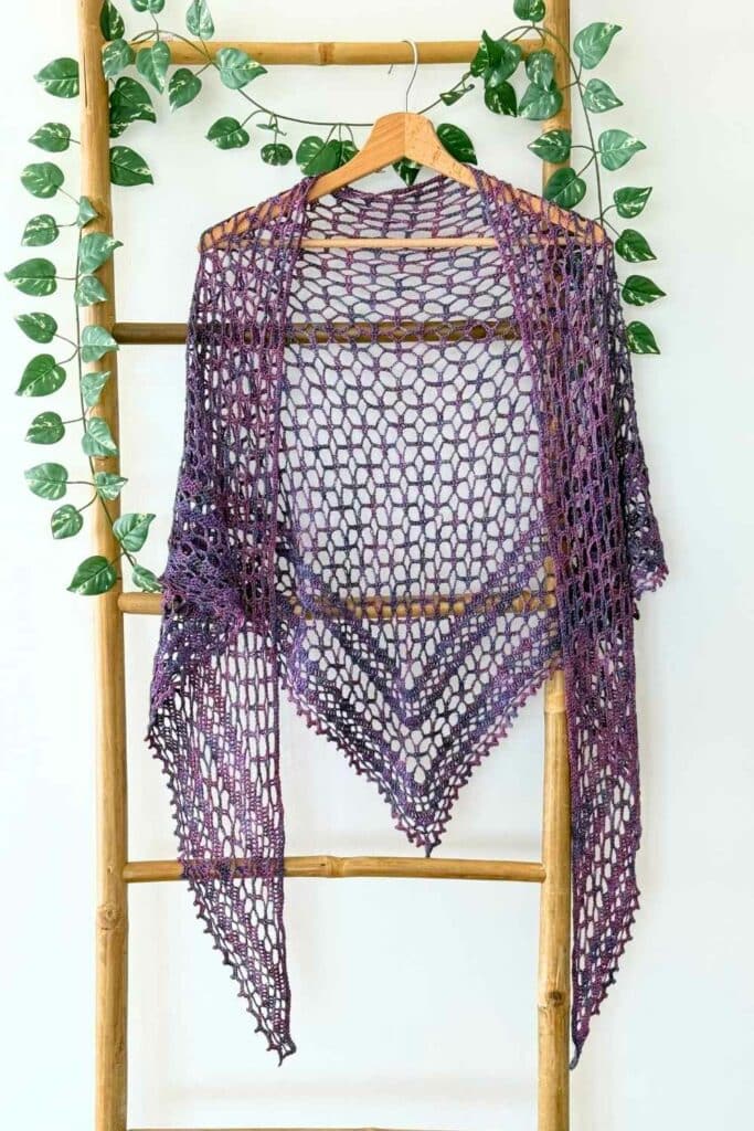 Nightfall lace crochet shawl displayed on a wooden ladder with greenery, showing the triangle shape and airy stitch pattern.