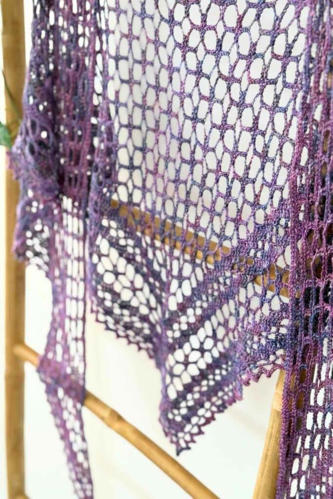 Close up of the Nightfall crochet shawl on a ladder, focusing on the lace stitches and the shifting purple color changes.