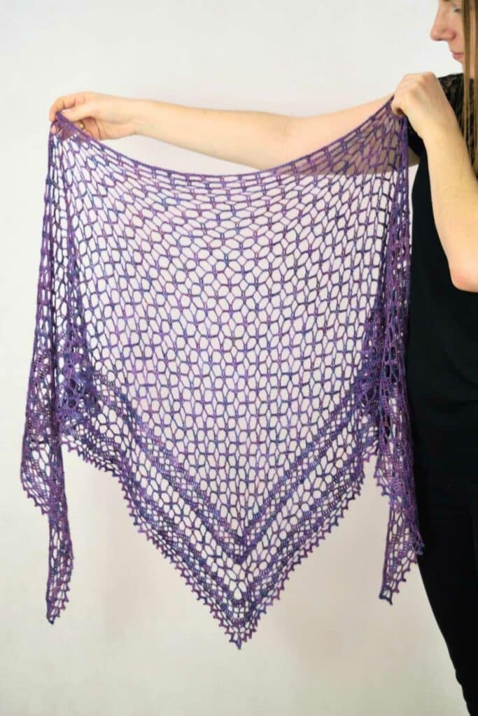 Nightfall crochet shawl held open by a person to show the full triangle shape, mesh lace texture, and lightweight drape.