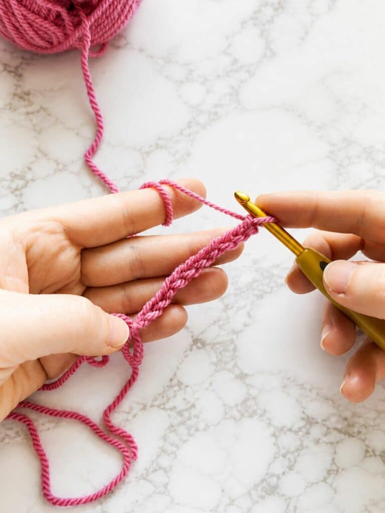Starting a back loop single crochet ribbing foundation chain with crochet hook and pink yarn
