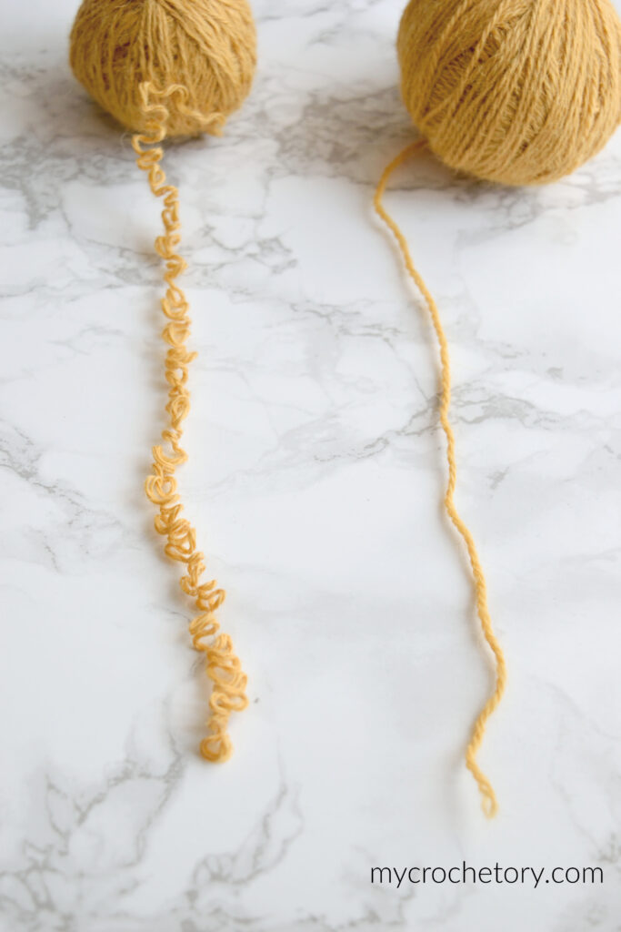 Frogged yarn before and after, a curly kinked strand of mustard yarn next to a smooth, straight one