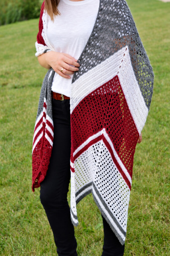 Red, white and gray crochet wrap draped loose over both shoulders, with the ends hanging down to the knees