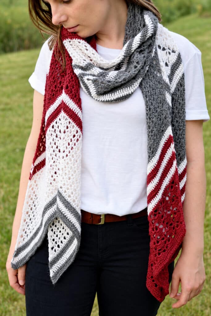 Woman looking down at her crochet wrap with white mesh lace and red and gray stripes