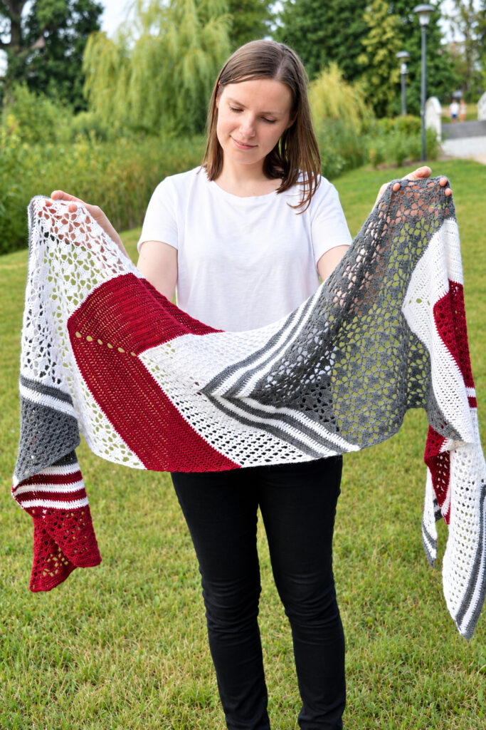 Woman holding the arrow crochet wrap open in both arms to show its full length and arrow shape