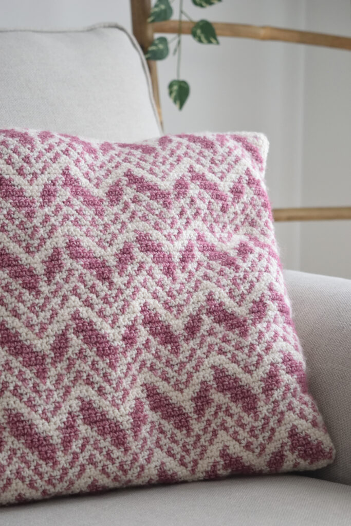 Cevro Intarsia Pillow with a pink and cream chevron pattern on a white sofa