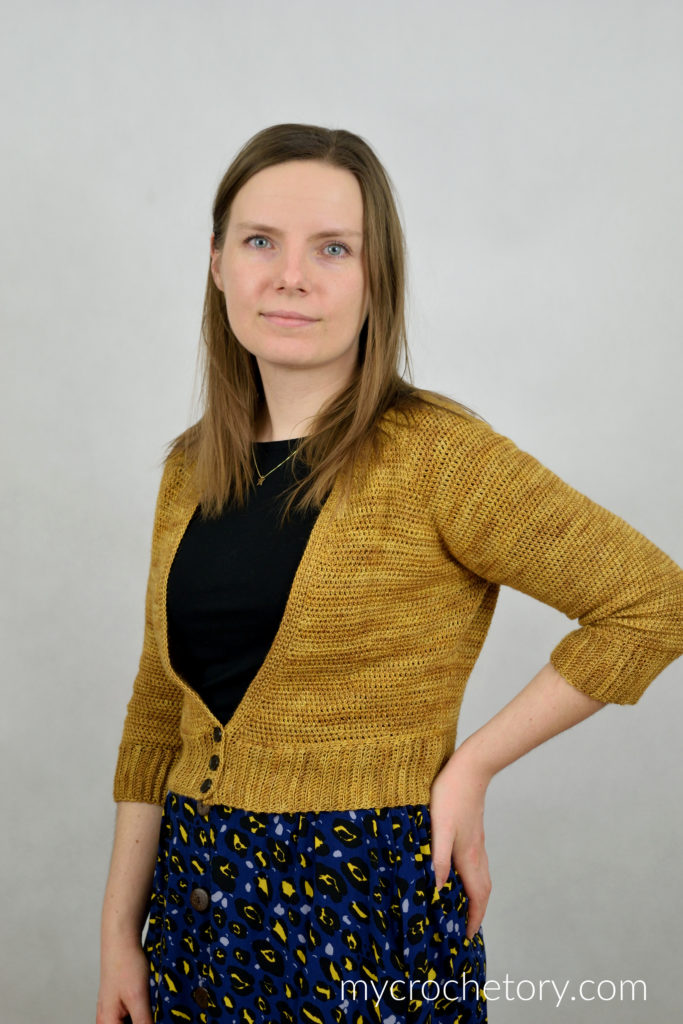 Rhea crochet cardigan in mustard yellow with a V-neck and buttons, worn over a black top