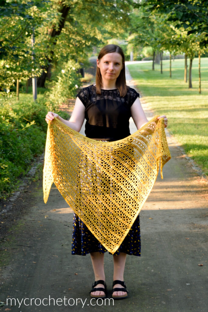 Gold crochet shawl held open in both arms to show the full triangle and the diagonal lace