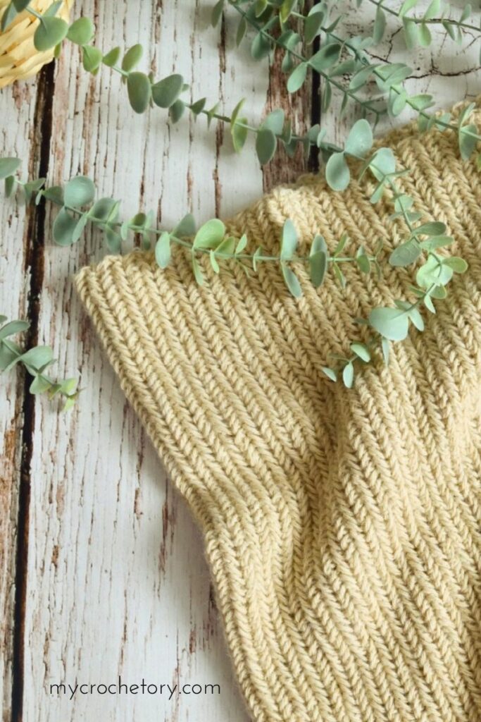Close up of textured herringbone crochet cowl on rustic wooden background, modern free crochet neck warmer pattern