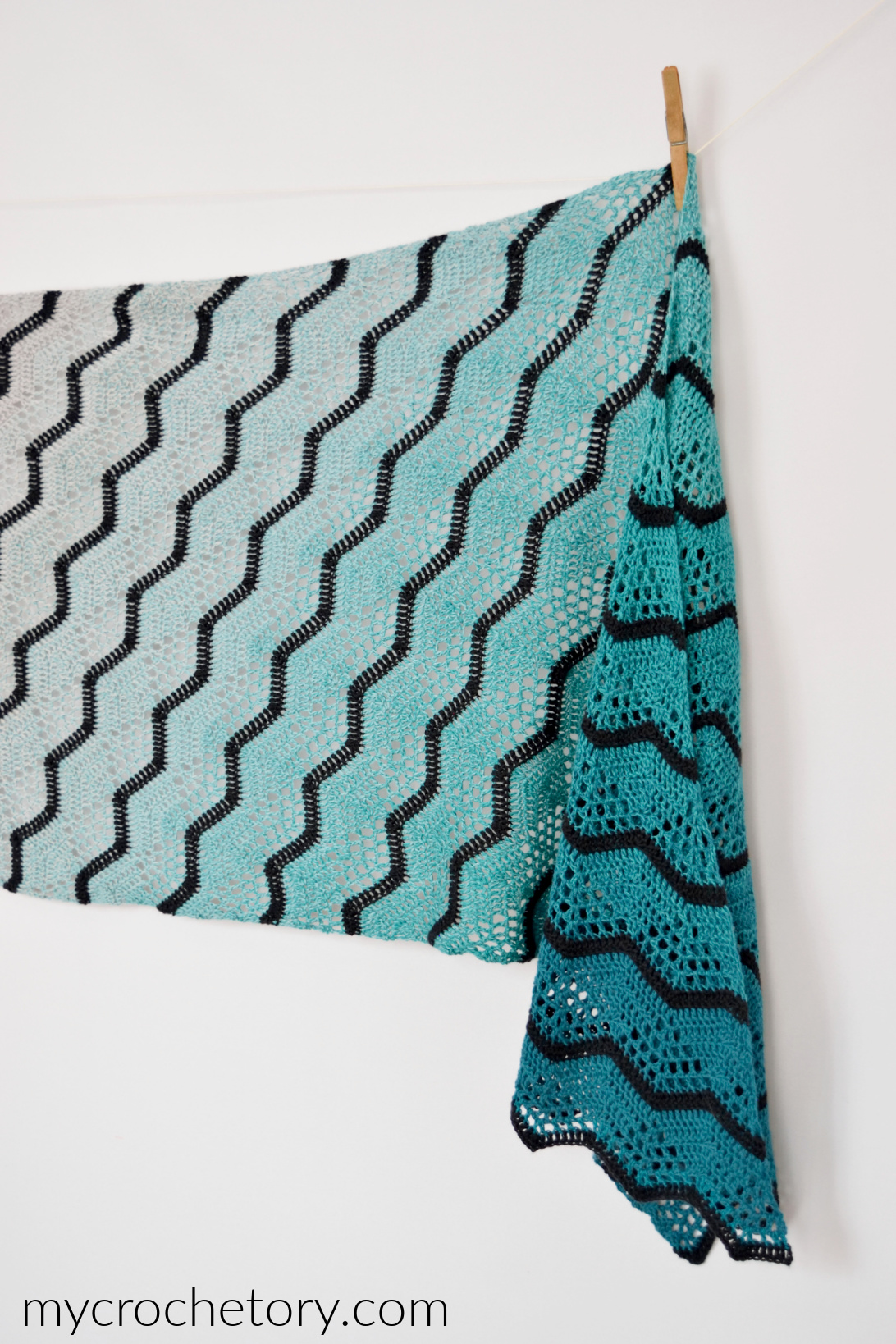 Havra ombre crochet wrap hanging flat, showing diagonal black chevron stripes over a gray to turquoise gradient