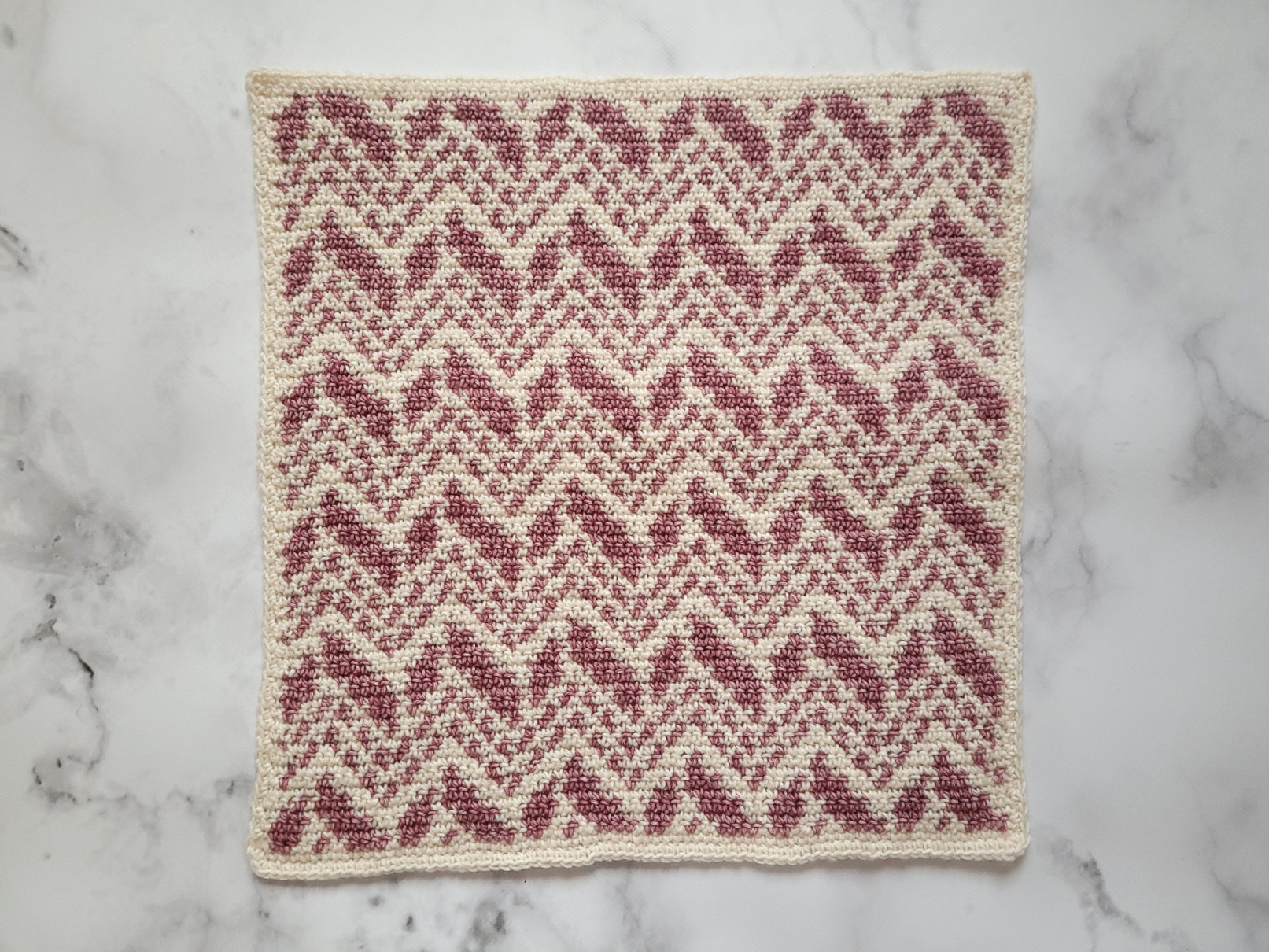 Finished front of the intarsia crochet pillow lying flat, cream and pink chevrons