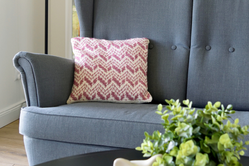 Cevro Intarsia Pillow, pink and white chevron crochet pillow on a gray armchair