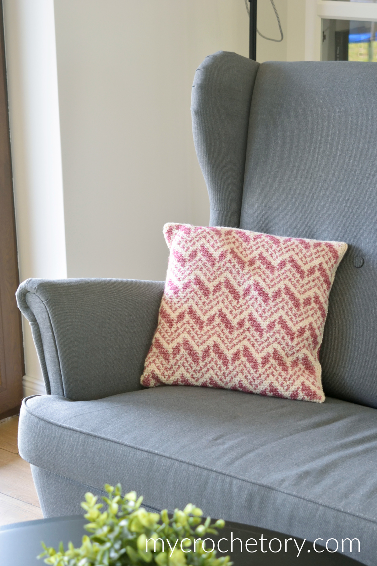 Close-up of the Cevro intarsia crochet pillow on a gray wingback armchair