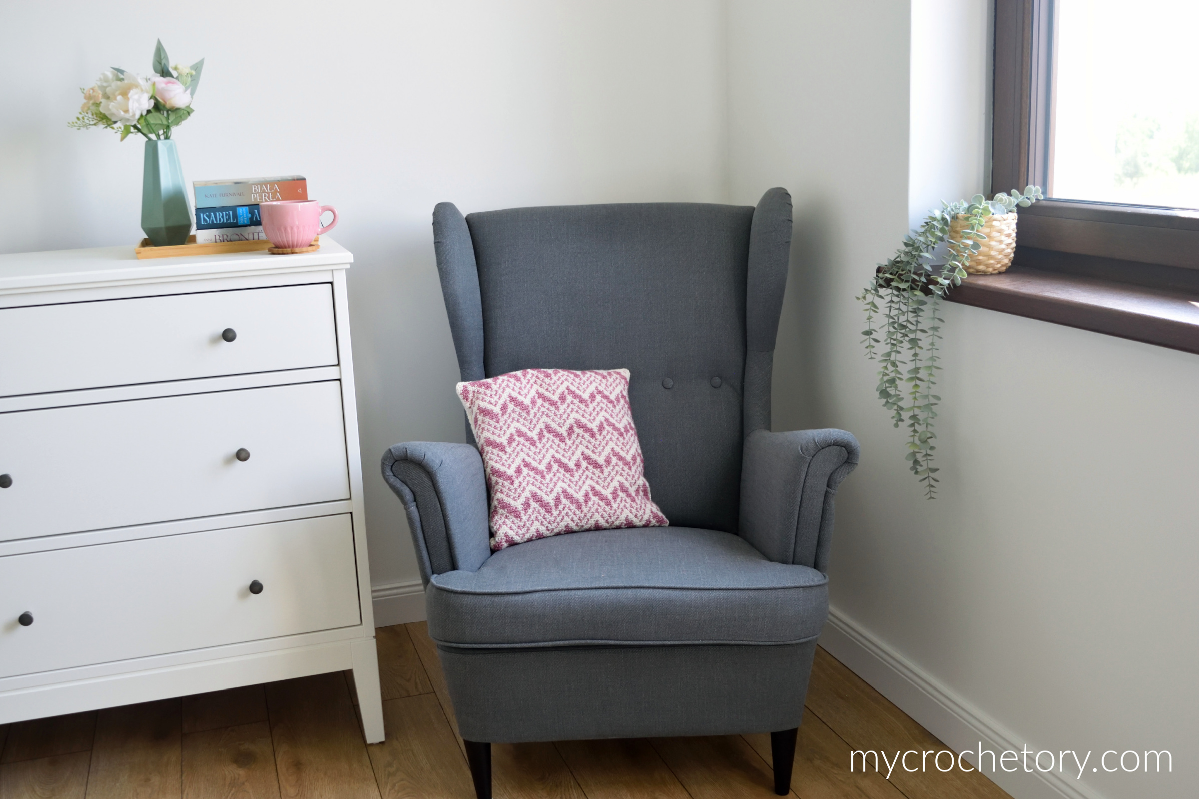 Intarsia crochet pillow on a gray armchair in the corner of a bright room