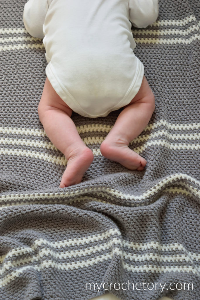 Baby lying on a handmade crochet blanket featuring the moss stitch, an easy example of beginning crochet stitches.