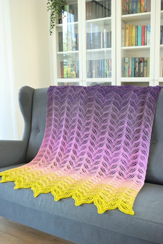 pink purple gradient crochet wave blanket draped over gray sofa showing lace ripple pattern