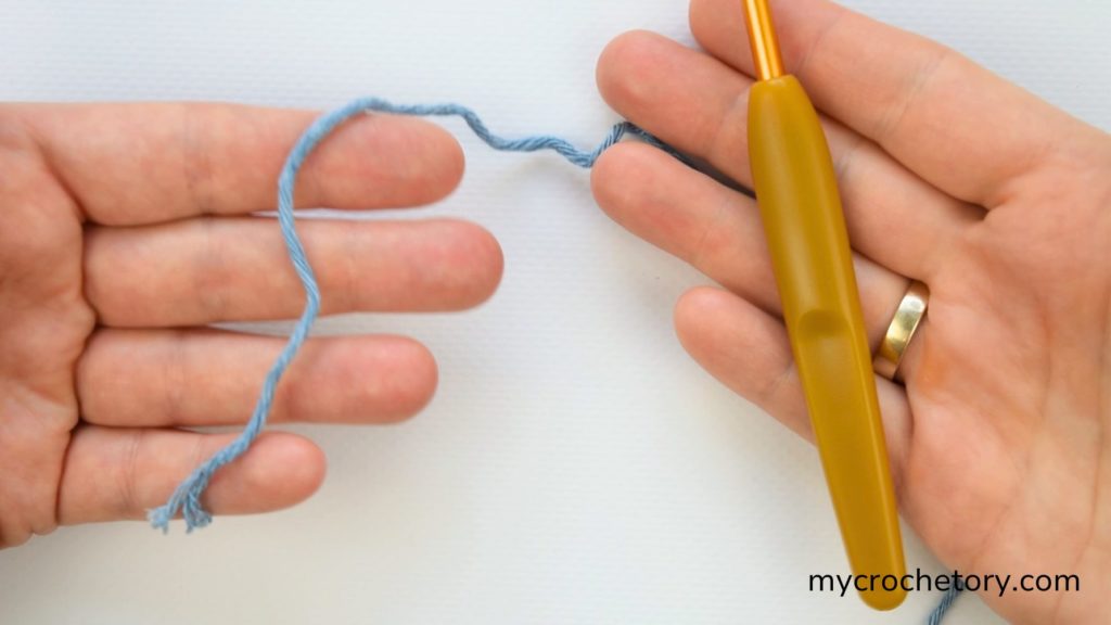 How do I crochet magic circle? This image shows the yarn tail and crochet hook setup for starting a magic ring.