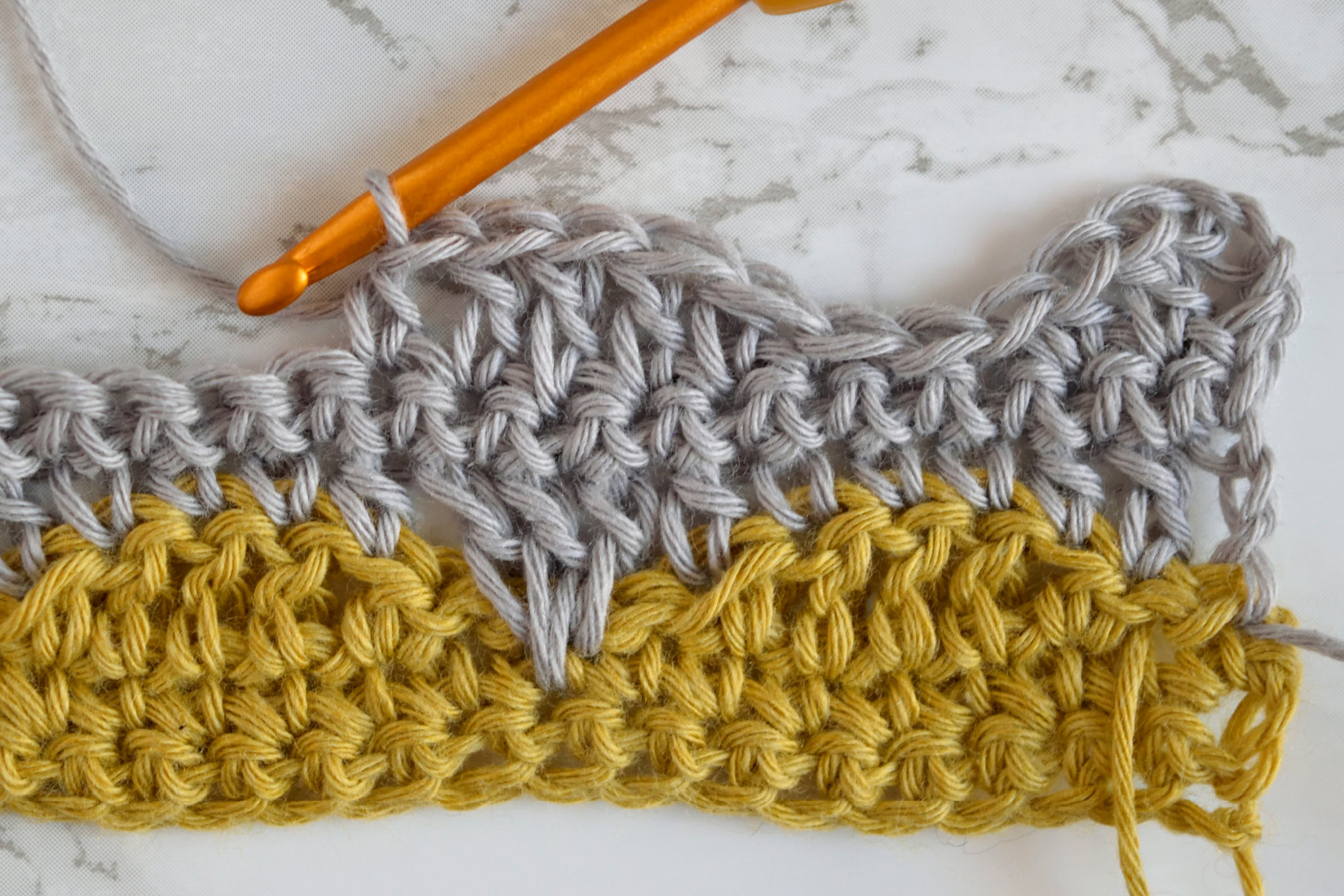 Gray row of the clamshell crochet stitch worked over a mustard row, with an orange crochet hook