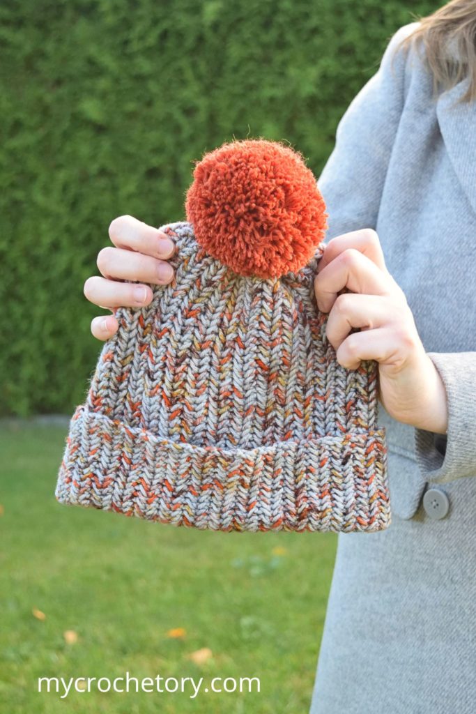 Hands holding a finished crochet winter hat pattern with a pom pom