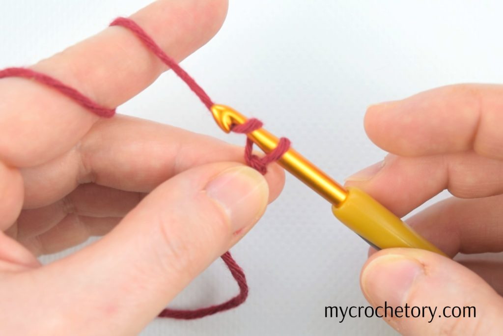 Hands demonstrating yarn over technique for crocheting a chain – learn how to crochet a chain effortlessly in our step-by-step guide!