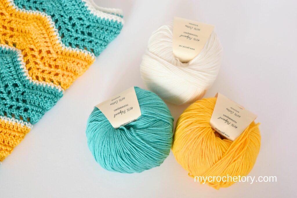 Three colorful balls of yarn next to a cozy blanket sample, illustrating the choice between crochet vs knitting yarn.