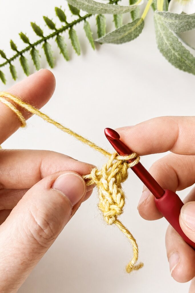 Hands working a crochet I-Cord with yellow yarn and a red crochet hook