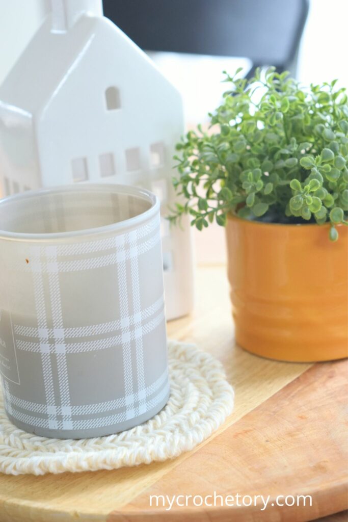 Modern home decor featuring a candle and plant on a herringbone round crochet coaster pattern.