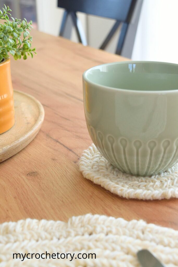 Green mug resting on a stylish round crochet coaster pattern with a herringbone stitch.