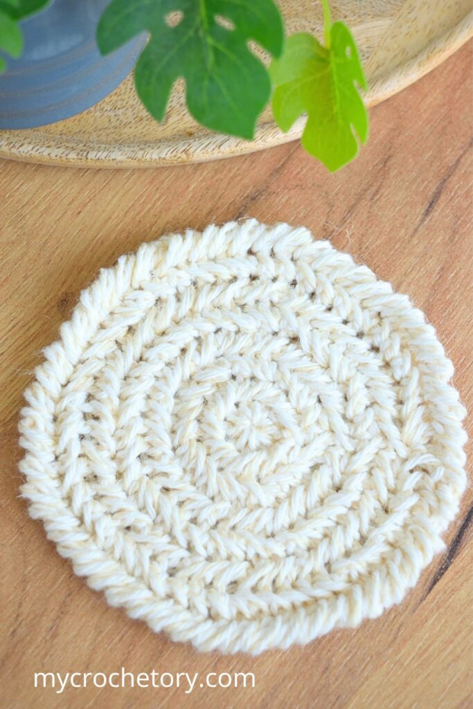 Flat-lay view of a detailed herringbone round crochet coaster pattern on a wooden table.