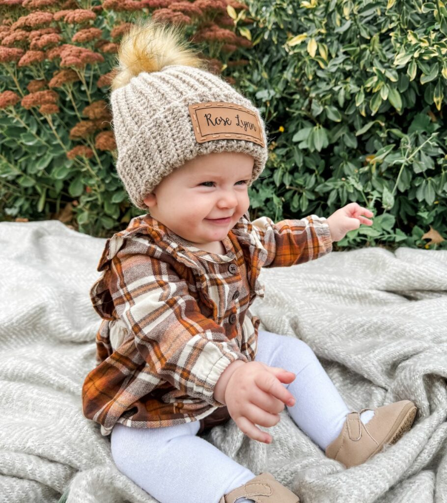 A happy baby wearing a soft beige hat with a fluffy pom-pom, showing cute infant crochet hat patterns.