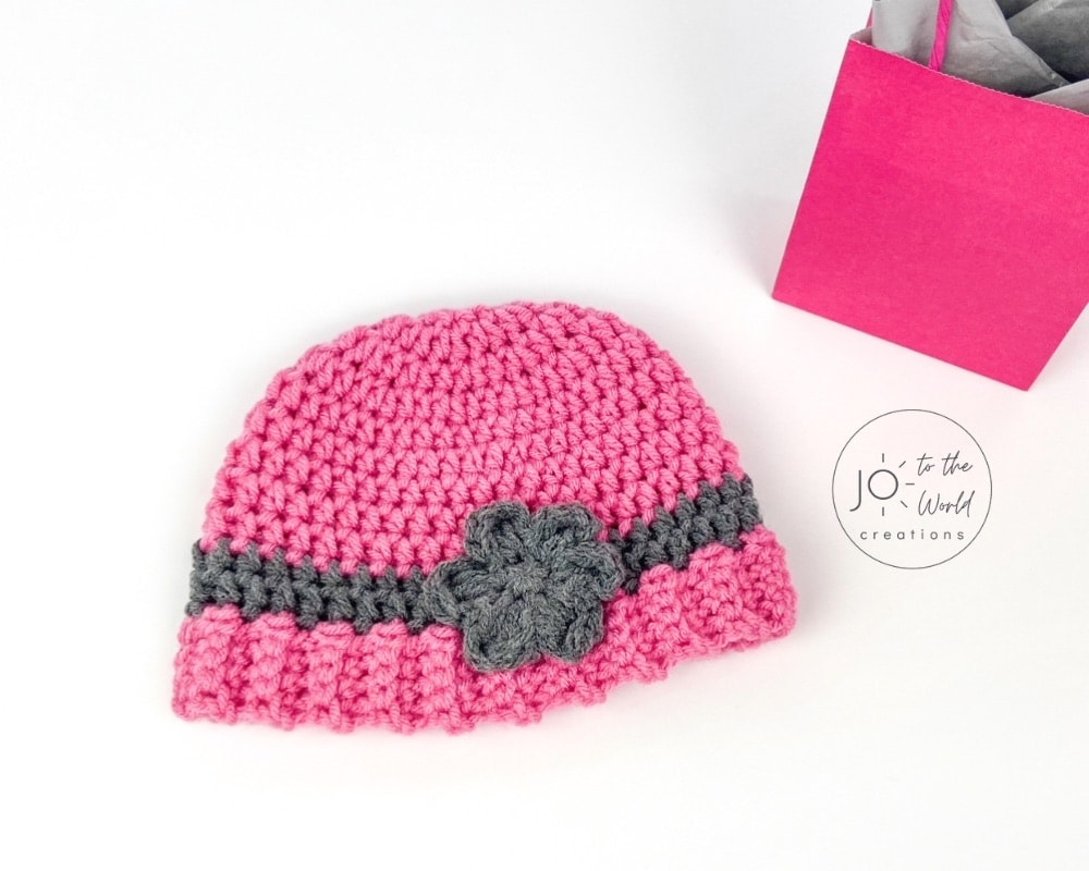 A bright pink crochet hat with a grey flower, perfect for infant crochet hat patterns.