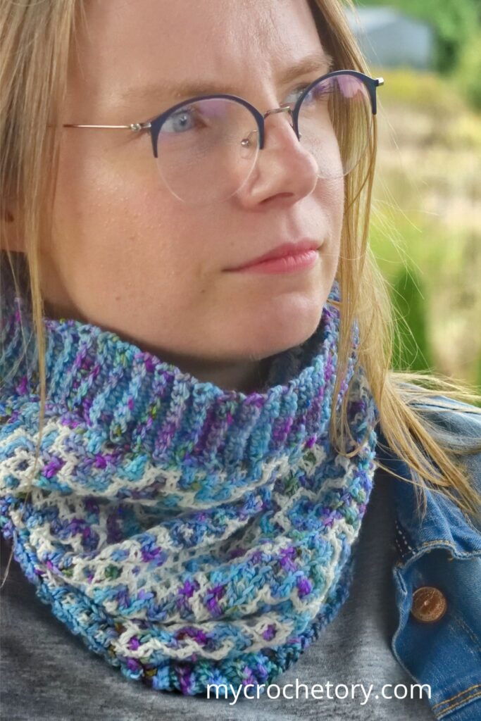 Side profile of a woman wearing the Drutozlot mosaic crochet cowl pattern, showing off the intricate colorwork.