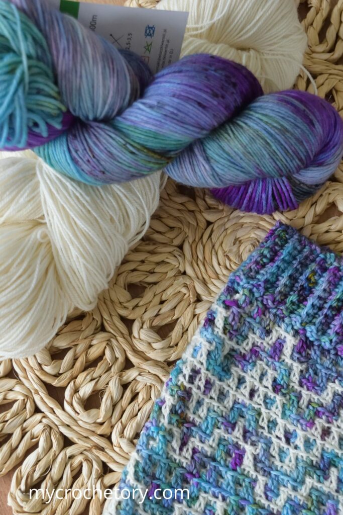 Close-up of colorful skeins of yarn used for the mosaic crochet cowl pattern, alongside the ribbed edge of the cowl.