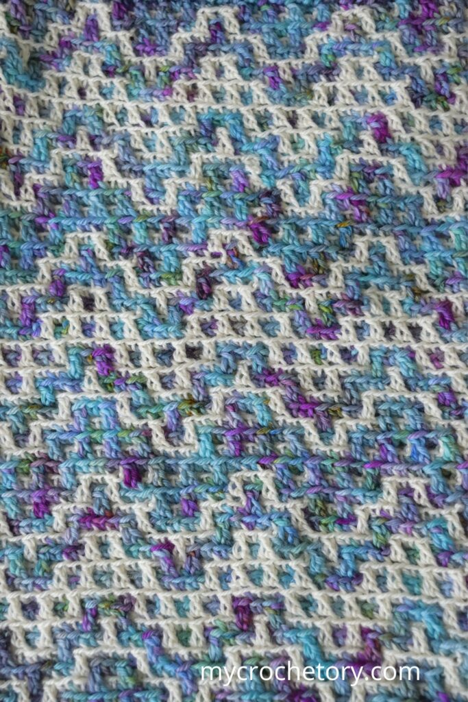 The Drutozlot mosaic crochet cowl pattern laid flat, showing the blue, purple, and white color pattern in close detail.