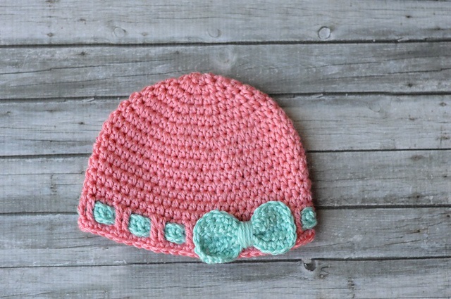 Infant crochet hat pattern featuring a pink beanie with a cute mint bow and decorative accents, ideal for stylish baby outfits.