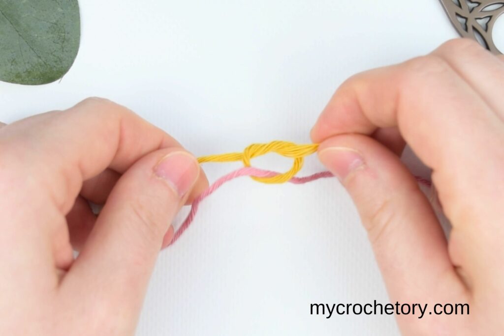 ightening the yellow yarn knot in the magic knot for joining yarn after looping it over and under the pink yarn.