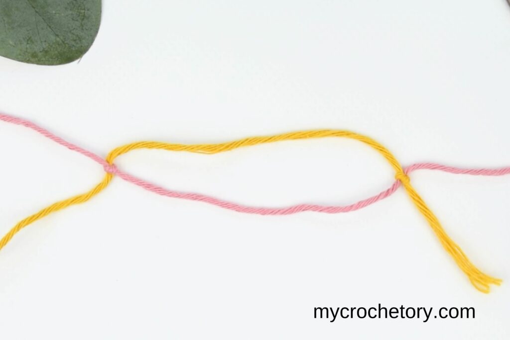 Pulling on the working yarn to bring both knots together in the magic knot for joining yarn.