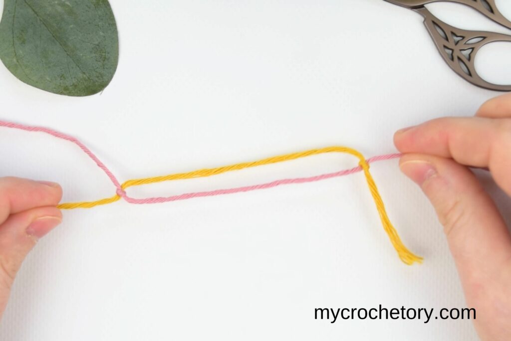 Hands pulling on the working yarn to ensure both knots meet in the middle for the magic knot for joining yarn.
