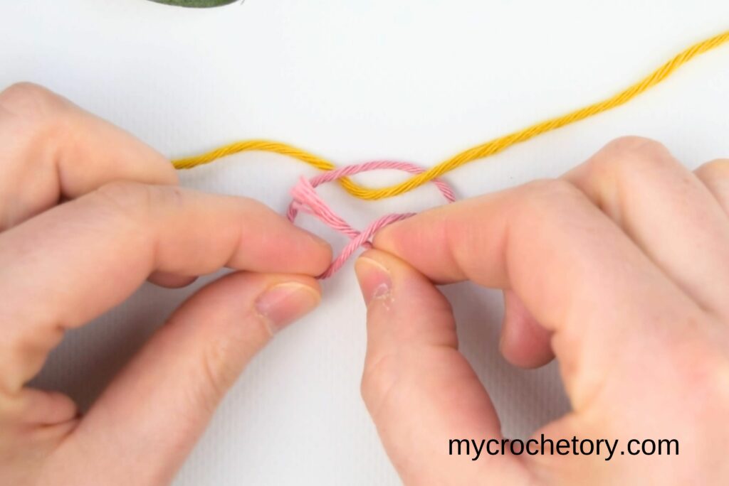 Hands pulling yarn strands to form the magic knot for joining yarn securely.